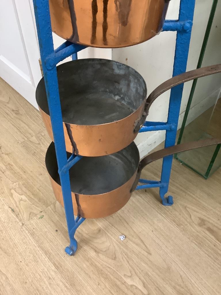 A graduating set of Victorian tin-lined copper saucepans (batterie de cuisine) on an associated tapering painted wrought iron stand